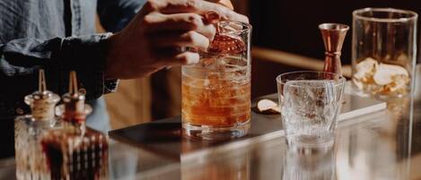 Un ambiente de bar con una persona sirviendo una bebida en un vaso, cubitos de hielo y diversas herramientas de bar.