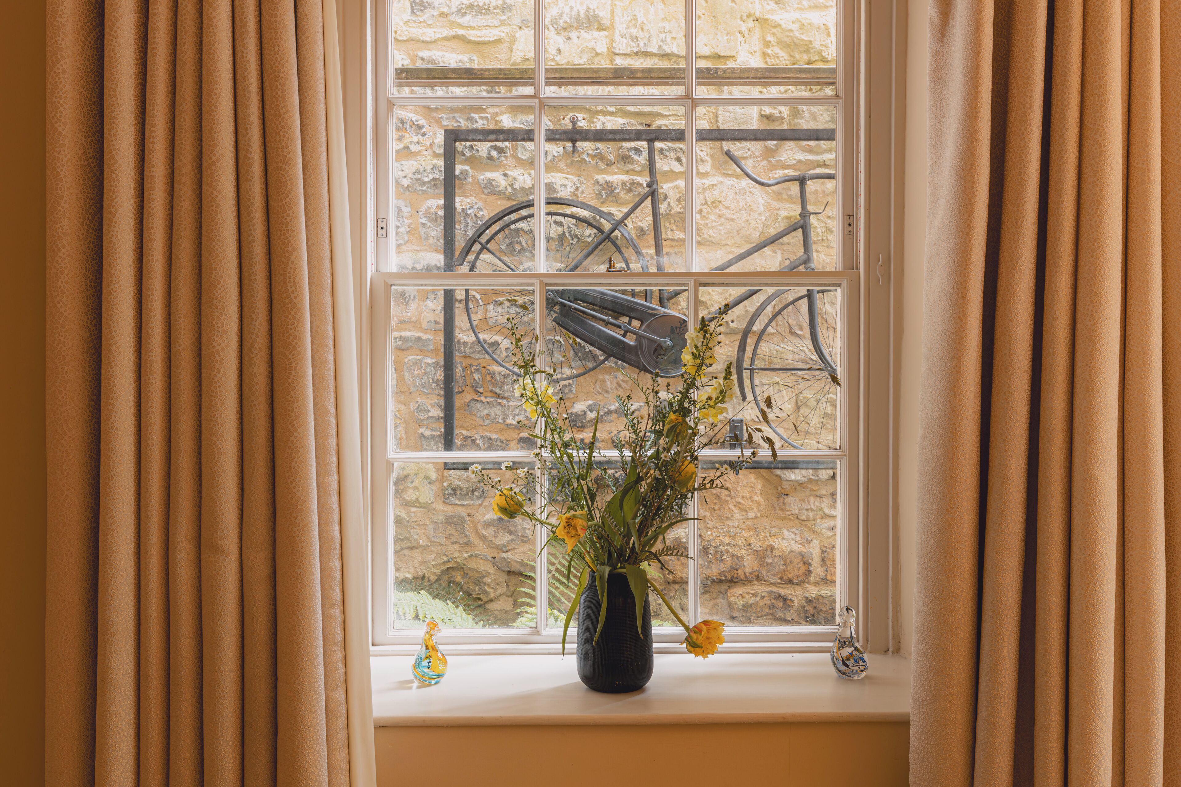 A window with a view of a stone wall and a bicycle.