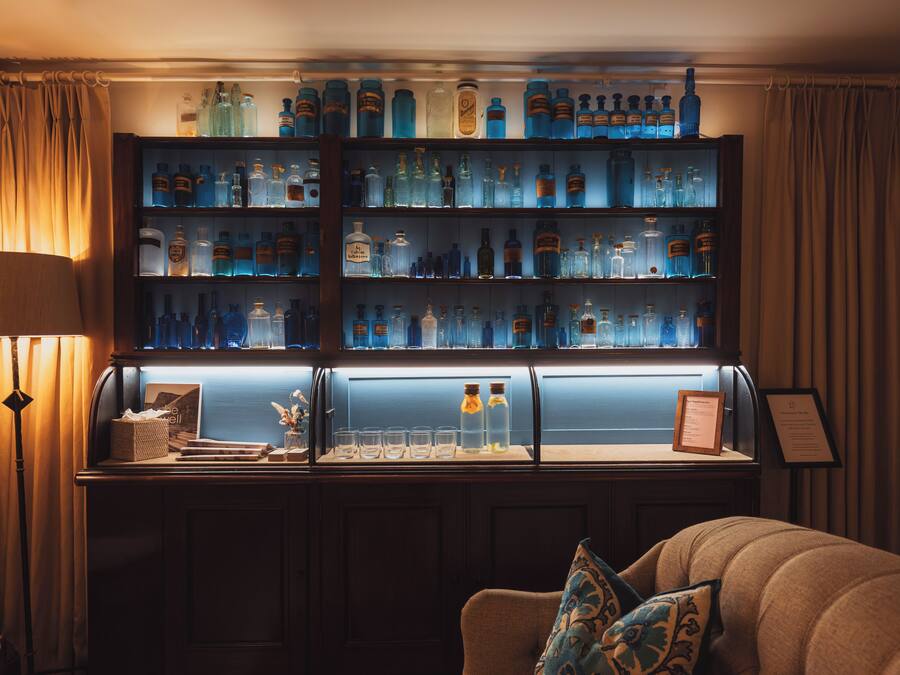 Eine Bar mit Regalen voller Flaschen und Gläsern, eine gepolsterte Sitzecke mit Lampe sowie eine Speisekarte im Rahmen auf der Theke.