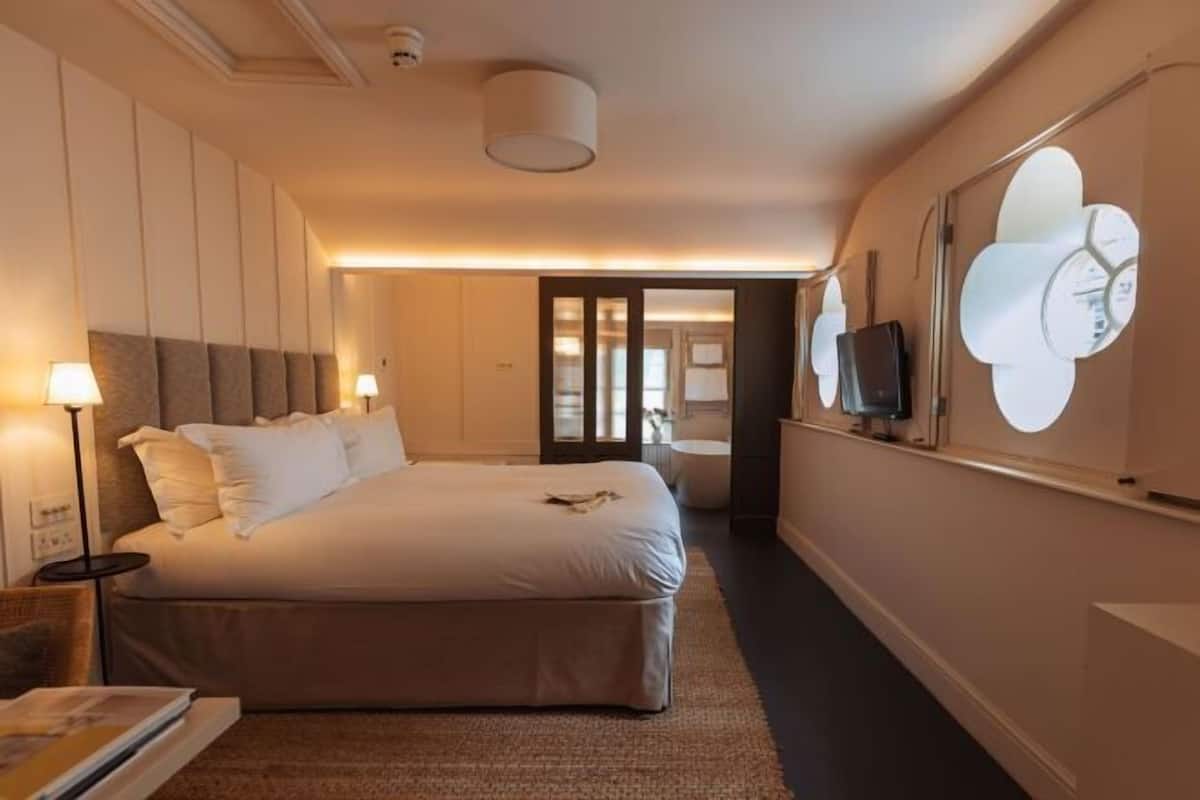 A hotel room with a large bed, bedside lamps, a flat-screen TV, and a wall-mounted clock.