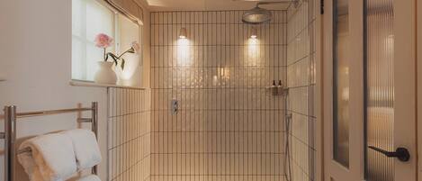 A bathroom with a shower, a towel rack with towels, and a window with flowers.