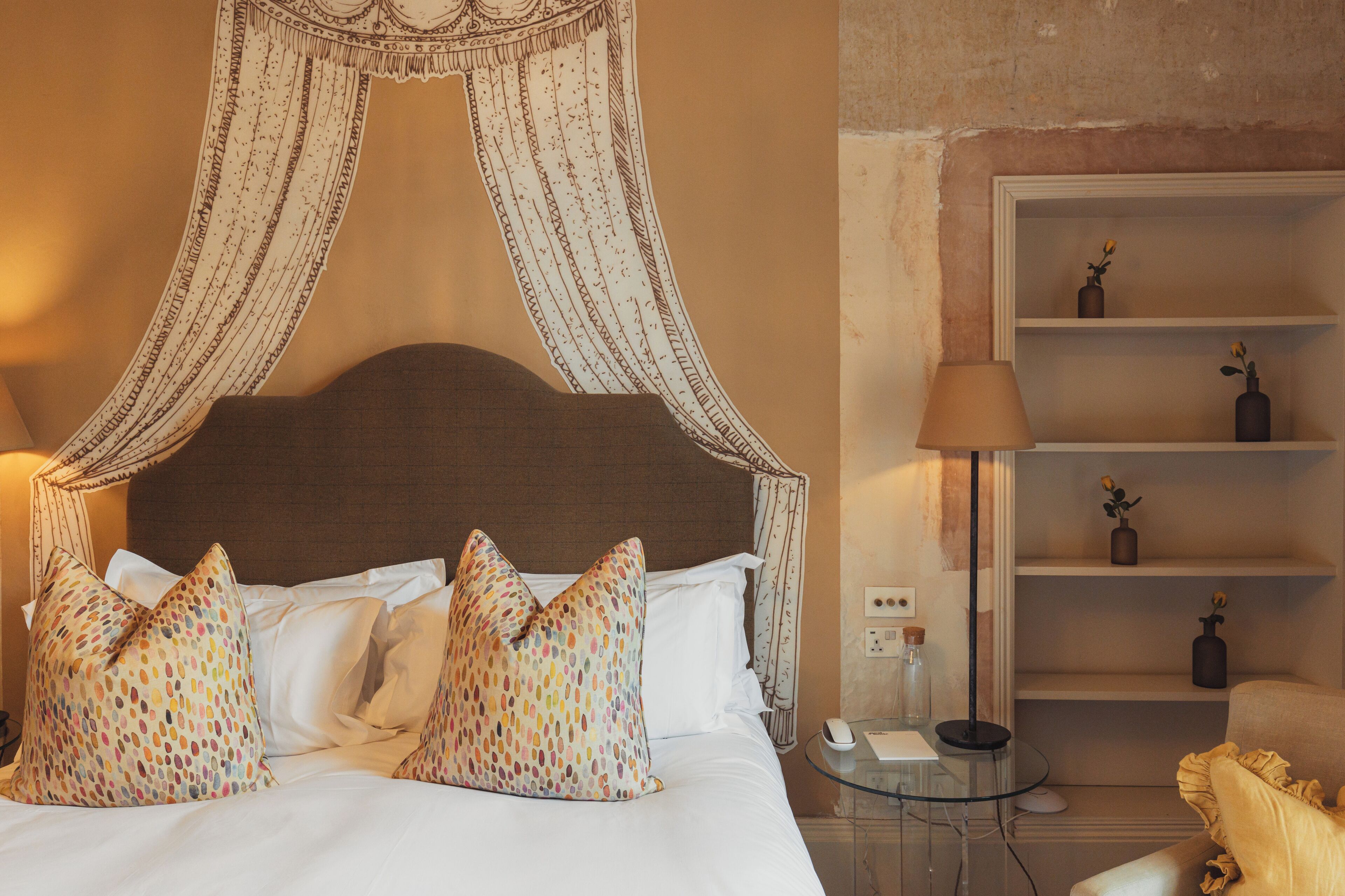 A neatly made bed with a canopy, a bedside table with a lamp, and a shelf with decorative items.