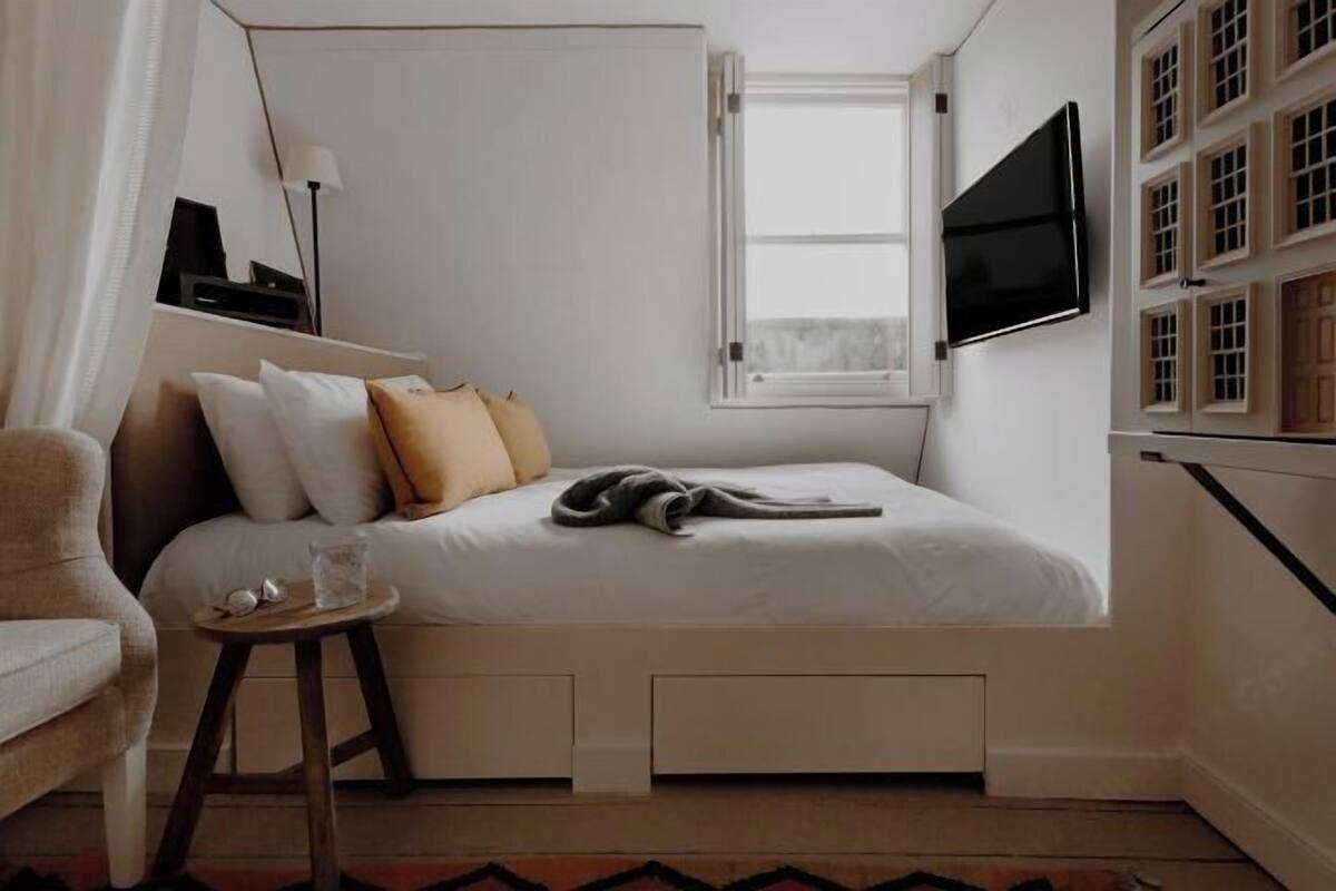 A bedroom with a bed, bedside table, lamp, TV, window, and built-in storage.
