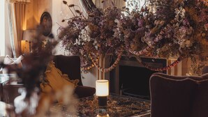 A cozy room with a plush sofa, a table with a lit lamp, and a decorative floral arrangement.