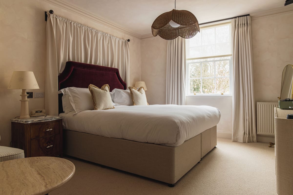 A bedroom with a large bed, bedside lamps, a nightstand, a round table, and a window with curtains.