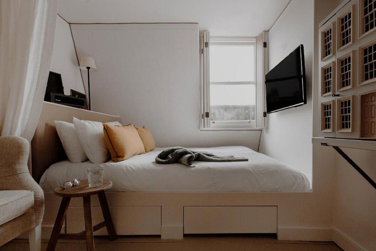 Une chambre à coucher avec un lit, une télévision, une fenêtre et une petite table.