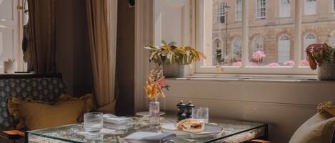Une table à manger avec un plateau en verre, un vase rempli de fleurs et un sandwich.