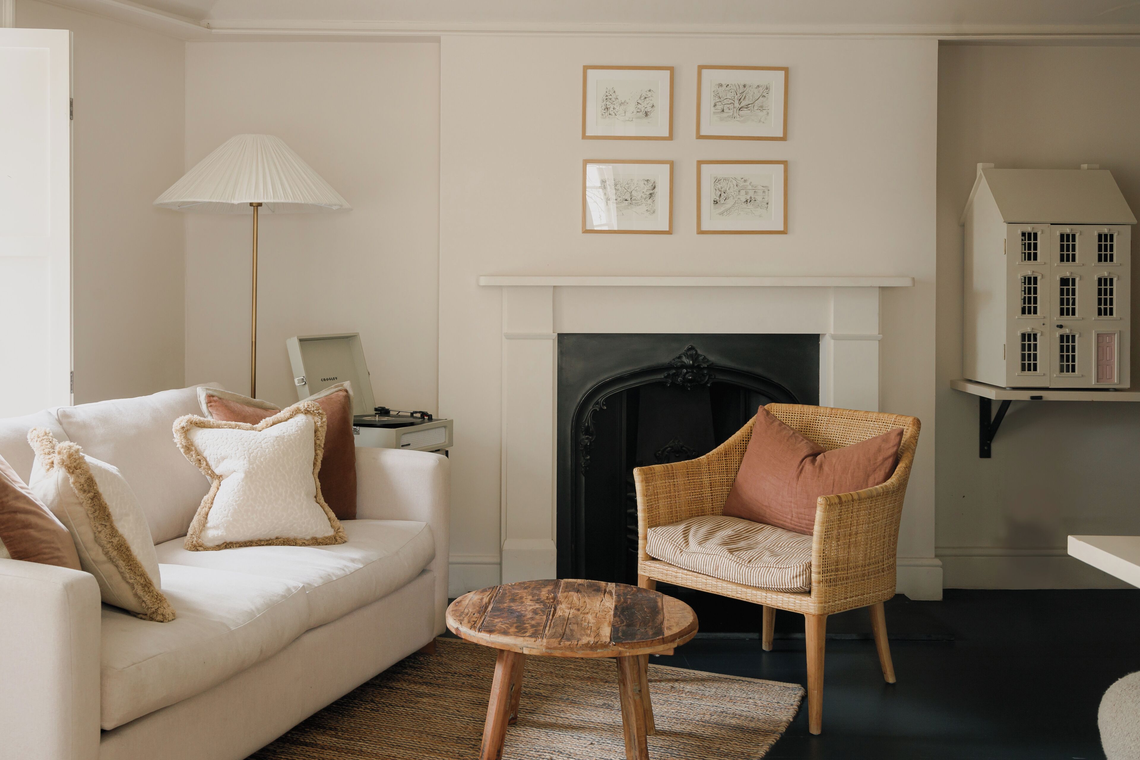 A living room with a white sofa, a wicker chair, a small wooden table, a fireplace, and framed artwork on the wall.