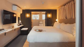 Une chambre d’hôtel avec un grand lit, une télévision, un bureau avec une lampe et une fenêtre avec des rideaux.