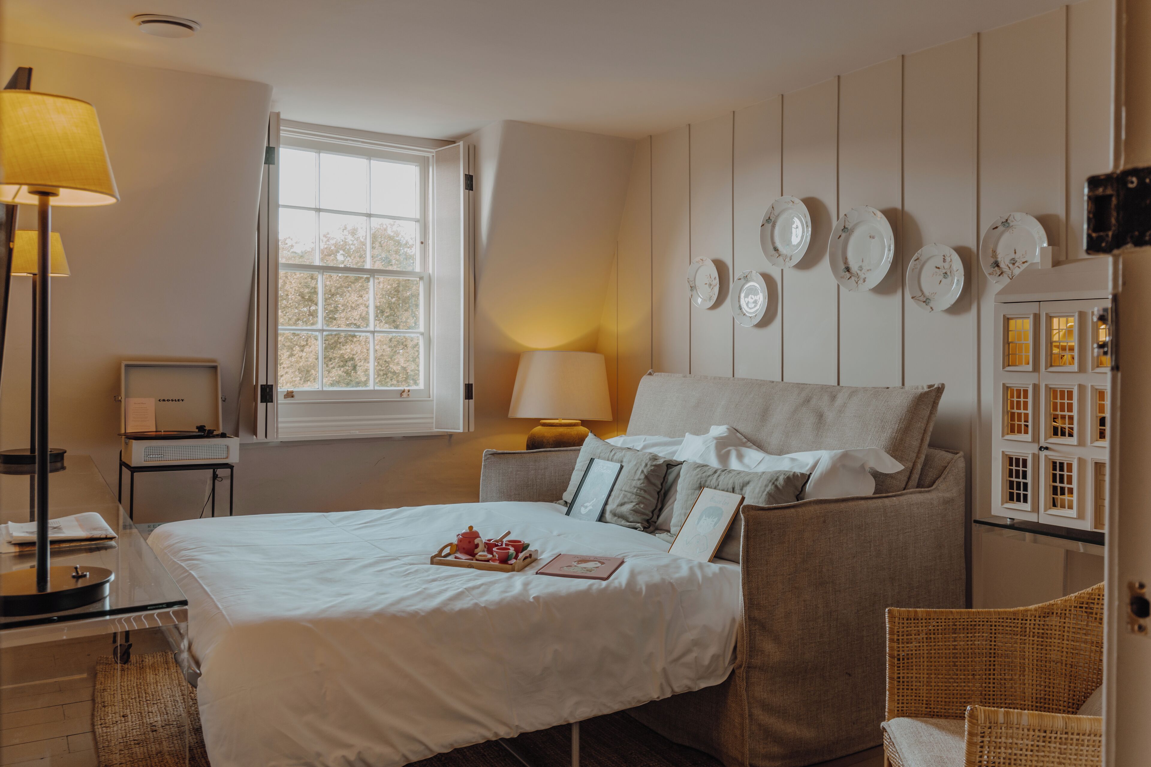 A neatly arranged bedroom with a bed, bedside table, lamp, and wall-mounted plates.