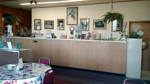 Enjoy meals at this restaurant with a cozy dining area and a counter featuring a clock, framed pictures, and a potted plant.
