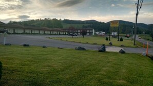 A parking lot with a building in the background, a grassy area in the foreground, and a sign with text. - Marlinton Motor Inn (Marlinton)