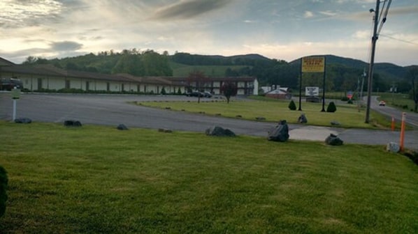 A parking lot with a building in the background, a grassy area in the foreground, and a sign with text.