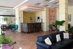 A hotel lobby with a reception desk, seating area, and potted plants. - Hotel Bellatrix (Macaé)