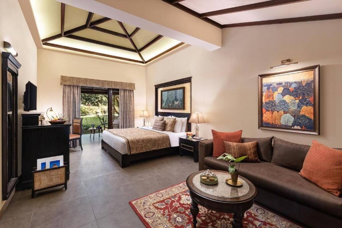 A hotel room with a bed, a sofa, a coffee table, a TV, and artwork on the walls.