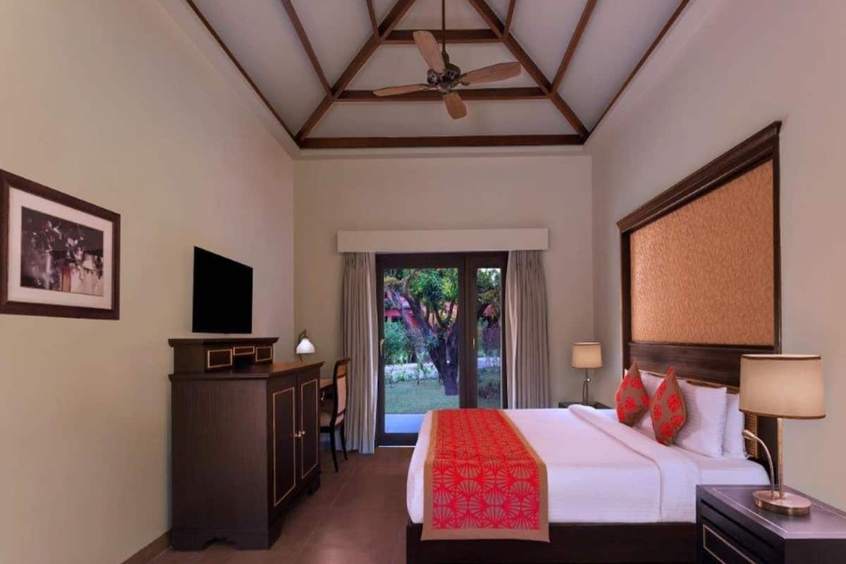 A hotel room with a bed, a desk, a television, a ceiling fan, and a view of the outdoors.