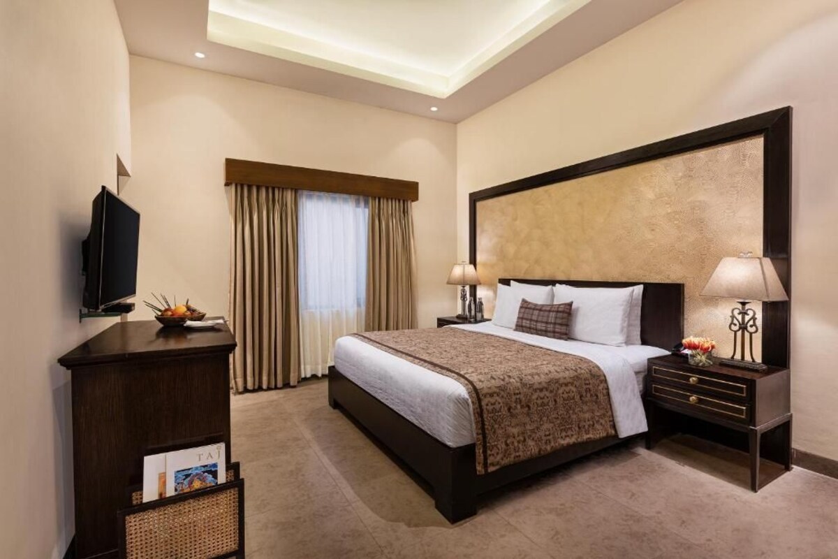 A hotel room with a large bed, a television, a desk, and a window with curtains.
