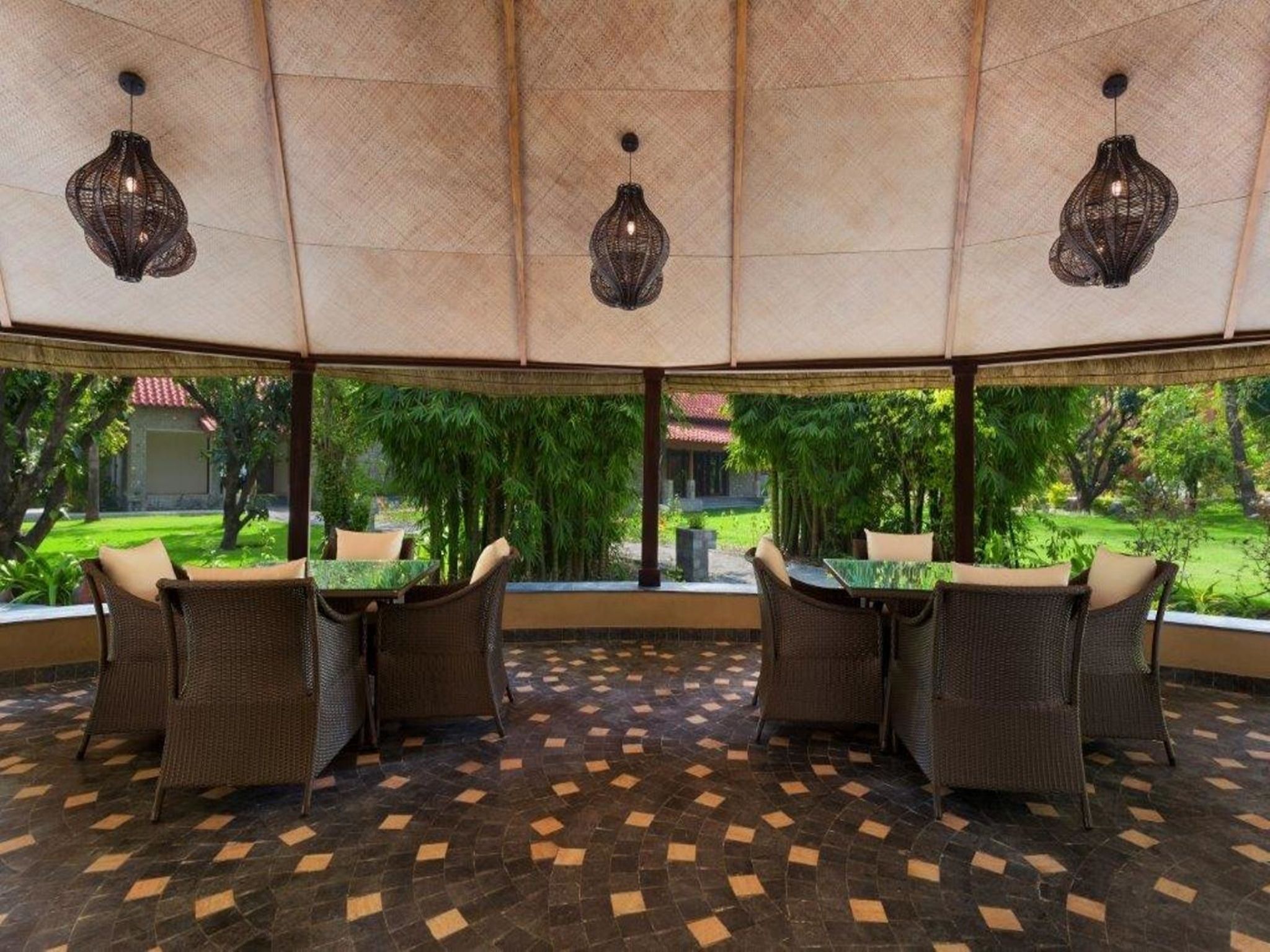 Un espacio al aire libre techado con mobiliario de mimbre y un suelo estampado, con vistas a un exuberante jardín.
