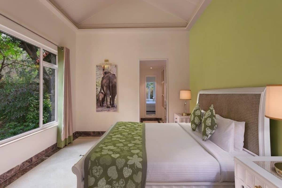 A hotel room with a large bed, a nightstand, a lamp, and a painting of elephants on the wall.