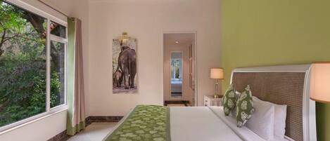 A hotel room with a large bed, a nightstand, a lamp, and a painting of elephants on the wall.