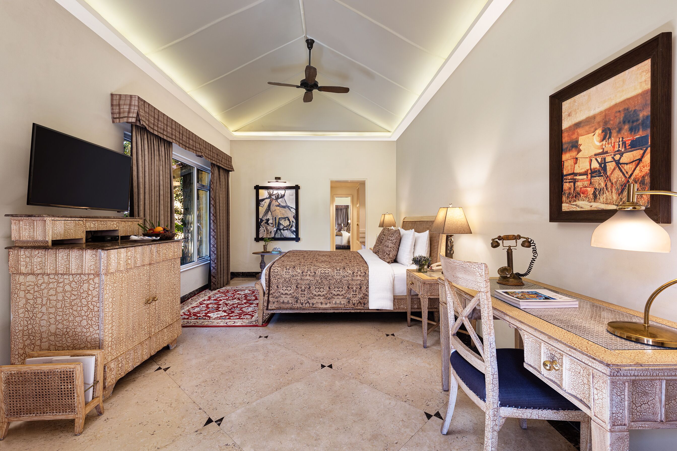 A hotel room with a bed, a desk, a television, and a ceiling fan.