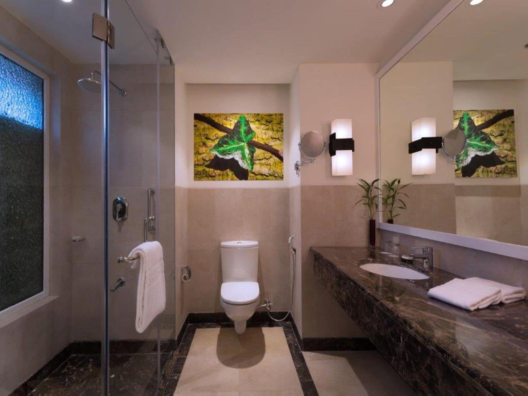 A modern bathroom with a glass shower enclosure, a toilet, a sink with a marble countertop, and a large mirror.