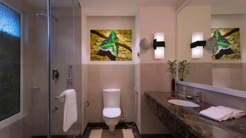 A modern bathroom with a glass shower enclosure, a toilet, a sink with a marble countertop, and a large mirror.