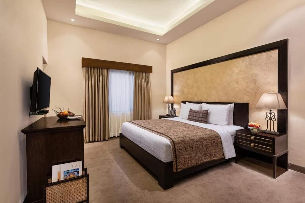 A hotel room with a large bed, a television, a desk, and a window with curtains.
