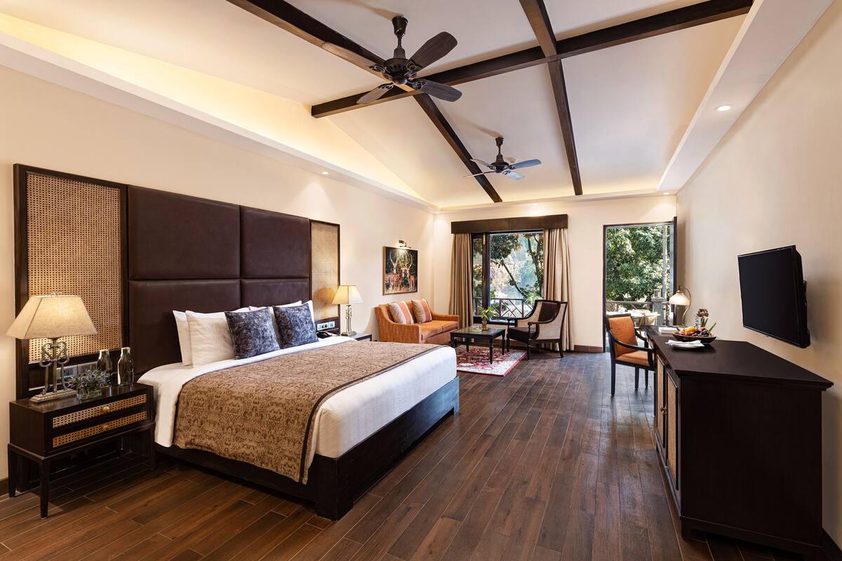 A modern hotel room with a large bed, a sofa, a dining area, and a TV.
