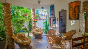 Un espacio interior acogedor con mobiliario de mimbre, un pilar de ladrillo y vistas a un jardín exuberante.