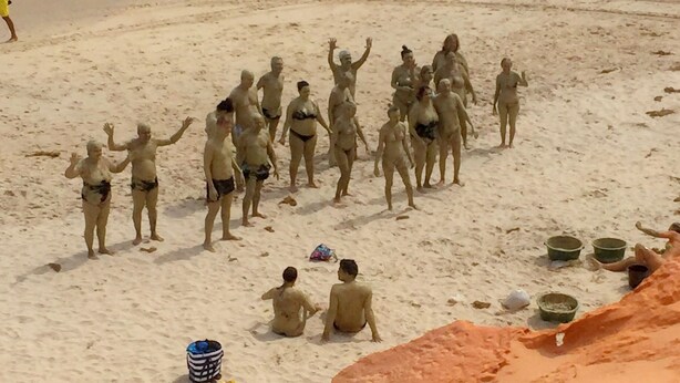 Una playa con gente de pie y sentada sobre la arena, algunos con cubos.