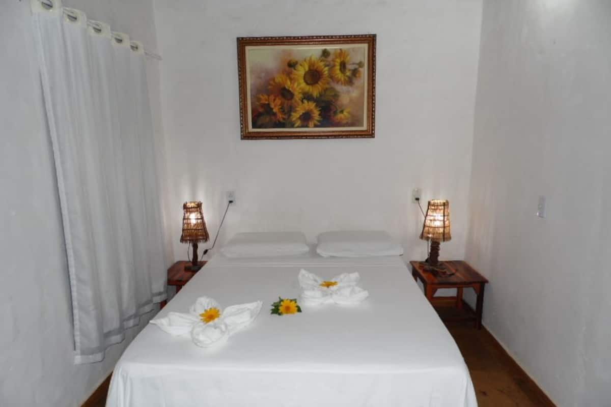 Una cama bien hecha con sábanas blancas, girasoles, dos lámparas de noche y un cuadro de girasoles en la pared.