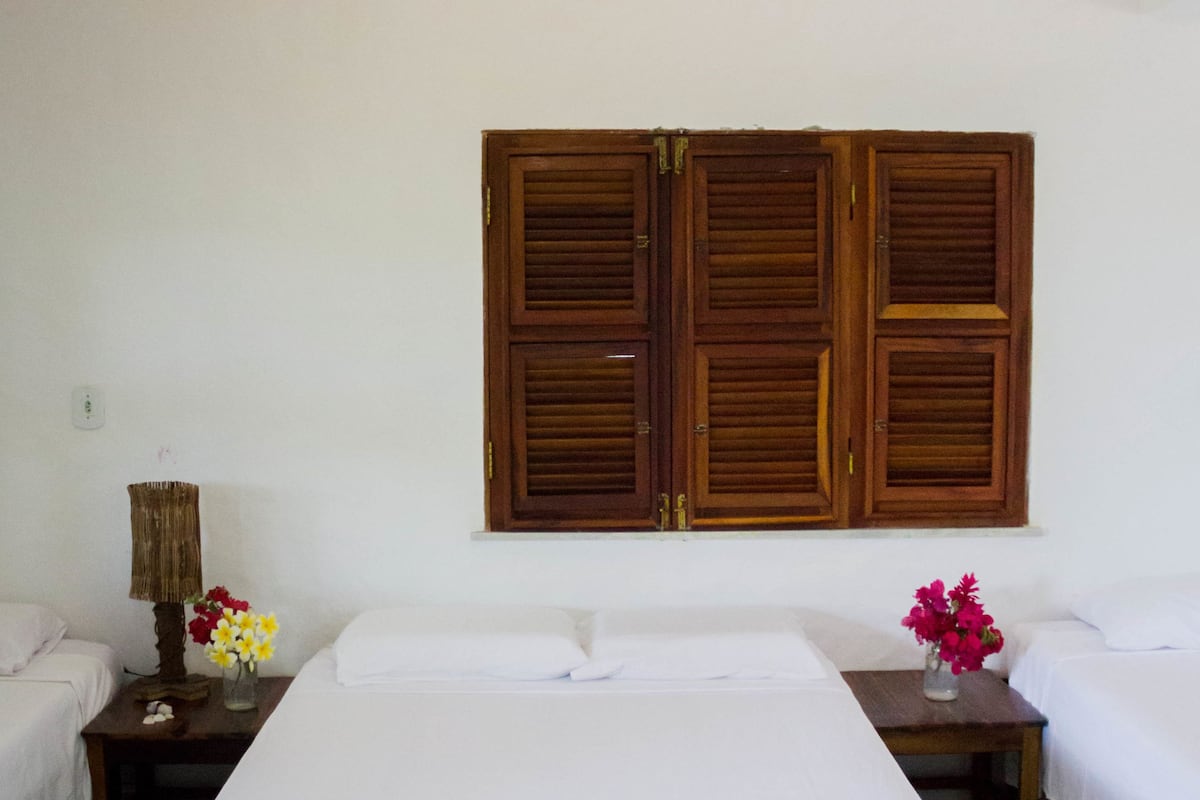 Una habitación de hotel con una cama grande, dos mesitas de noche, contraventanas de madera y una lámpara colgante.