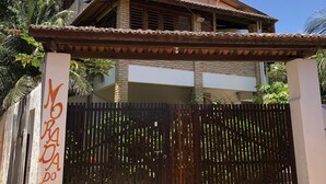 Una casa de dos pisos con entrada protegida por un portón, un balcón y un cartel con texto.