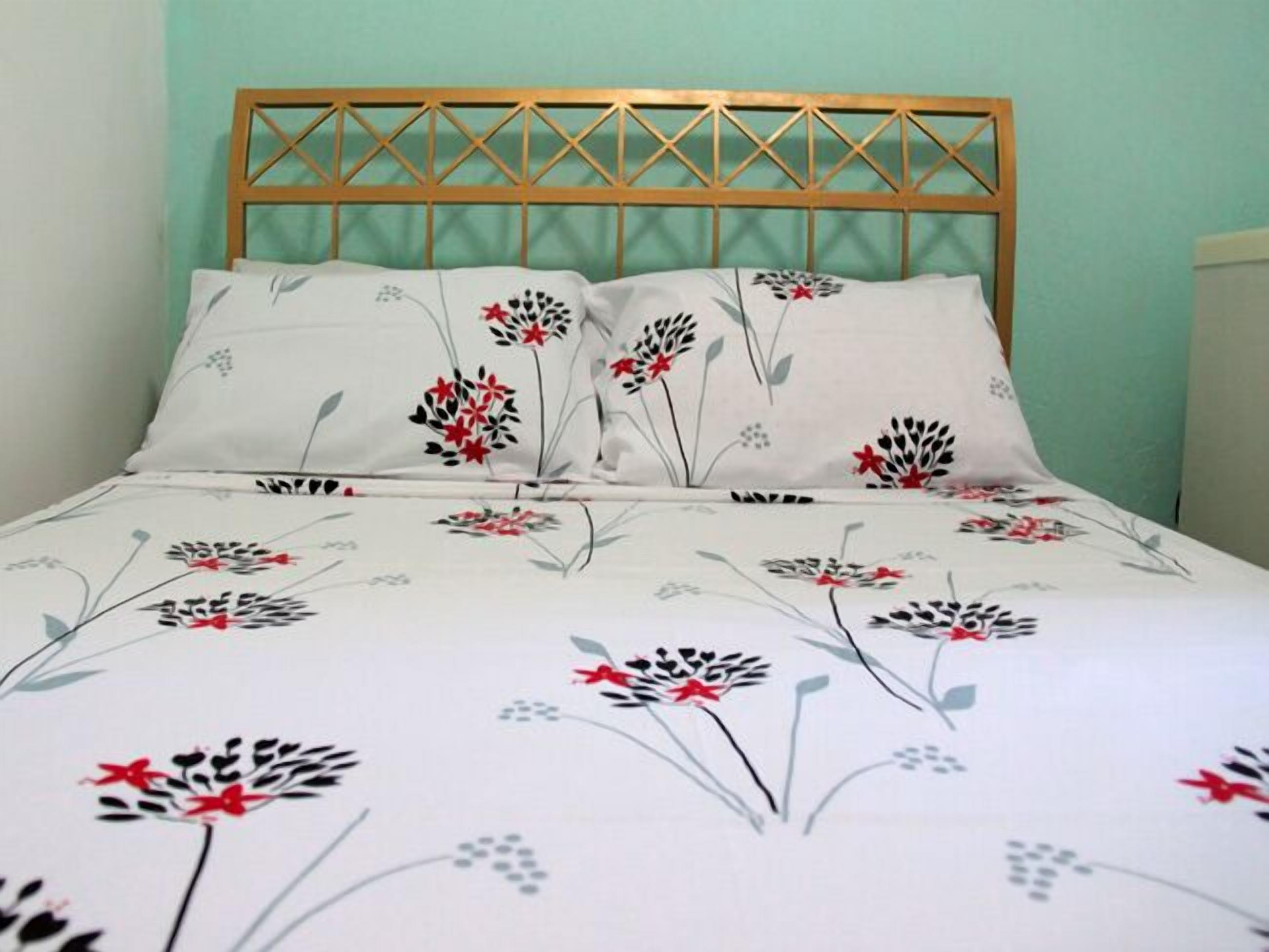 A bed with a floral-patterned bedspread and pillows, a wooden headboard, and a light green wall.