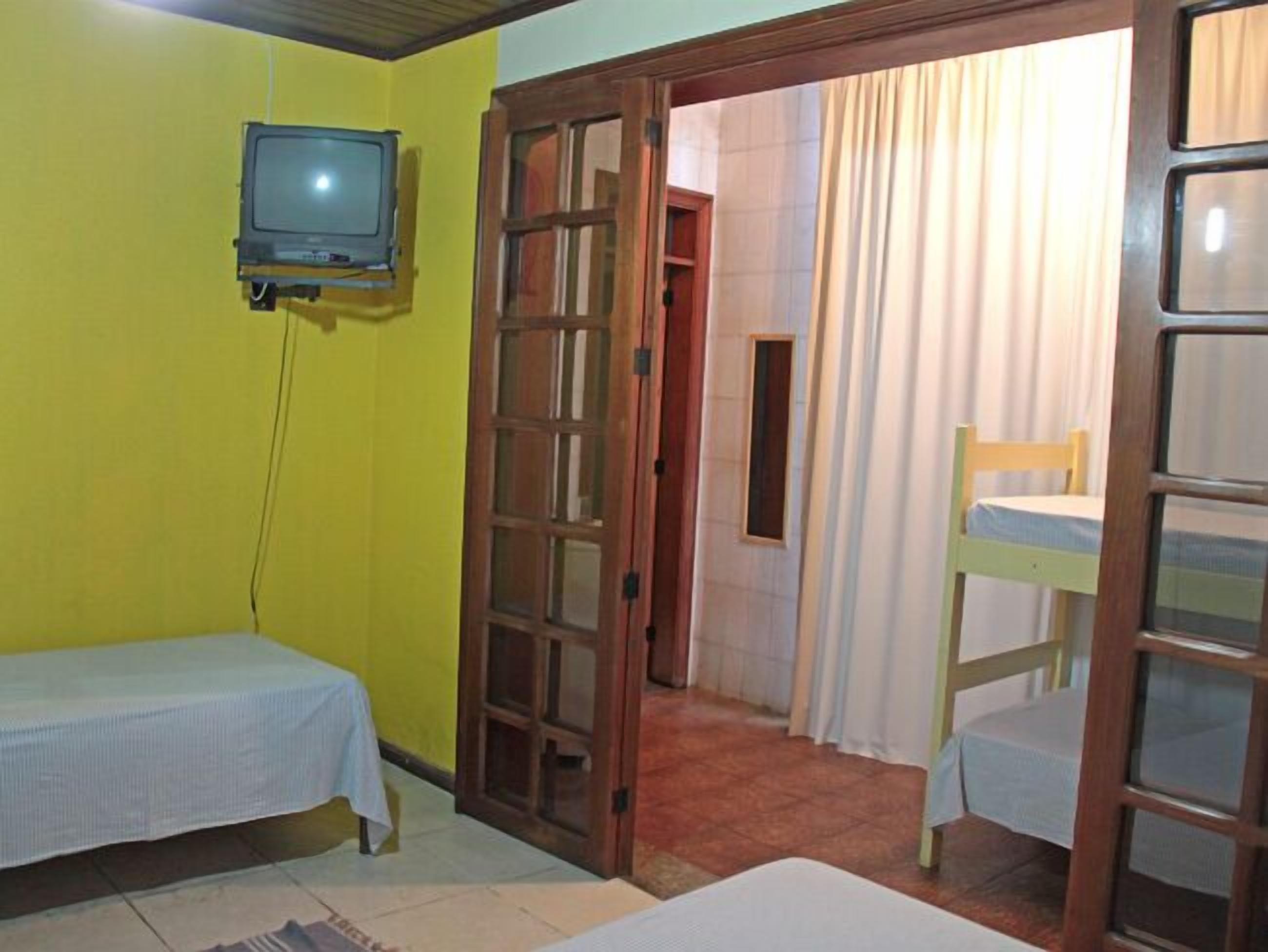 A small room with a bed, a table, a chair, and a television on the wall.
