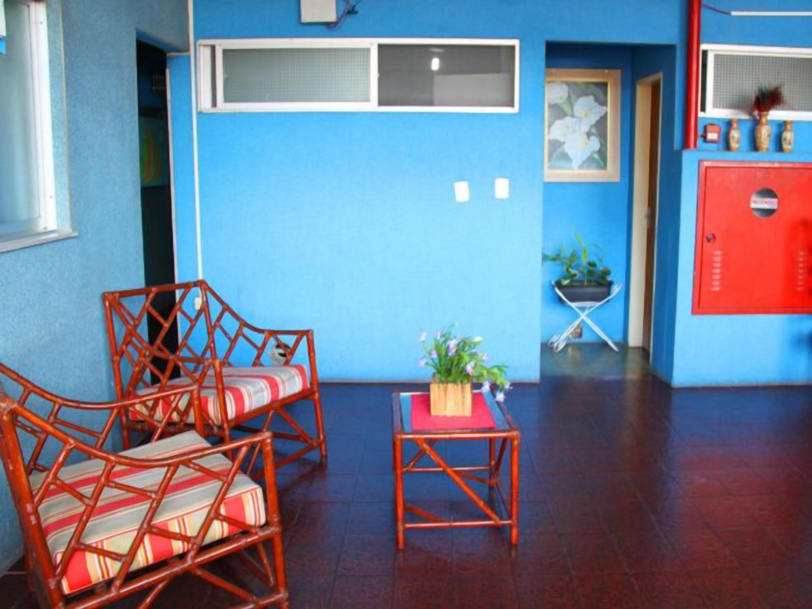 Una habitación con dos sillas de mimbre, una mesita con una planta y un armario rojo.