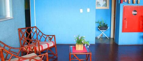 Una habitación con dos sillas de mimbre, una mesita con una planta y un armario rojo.
