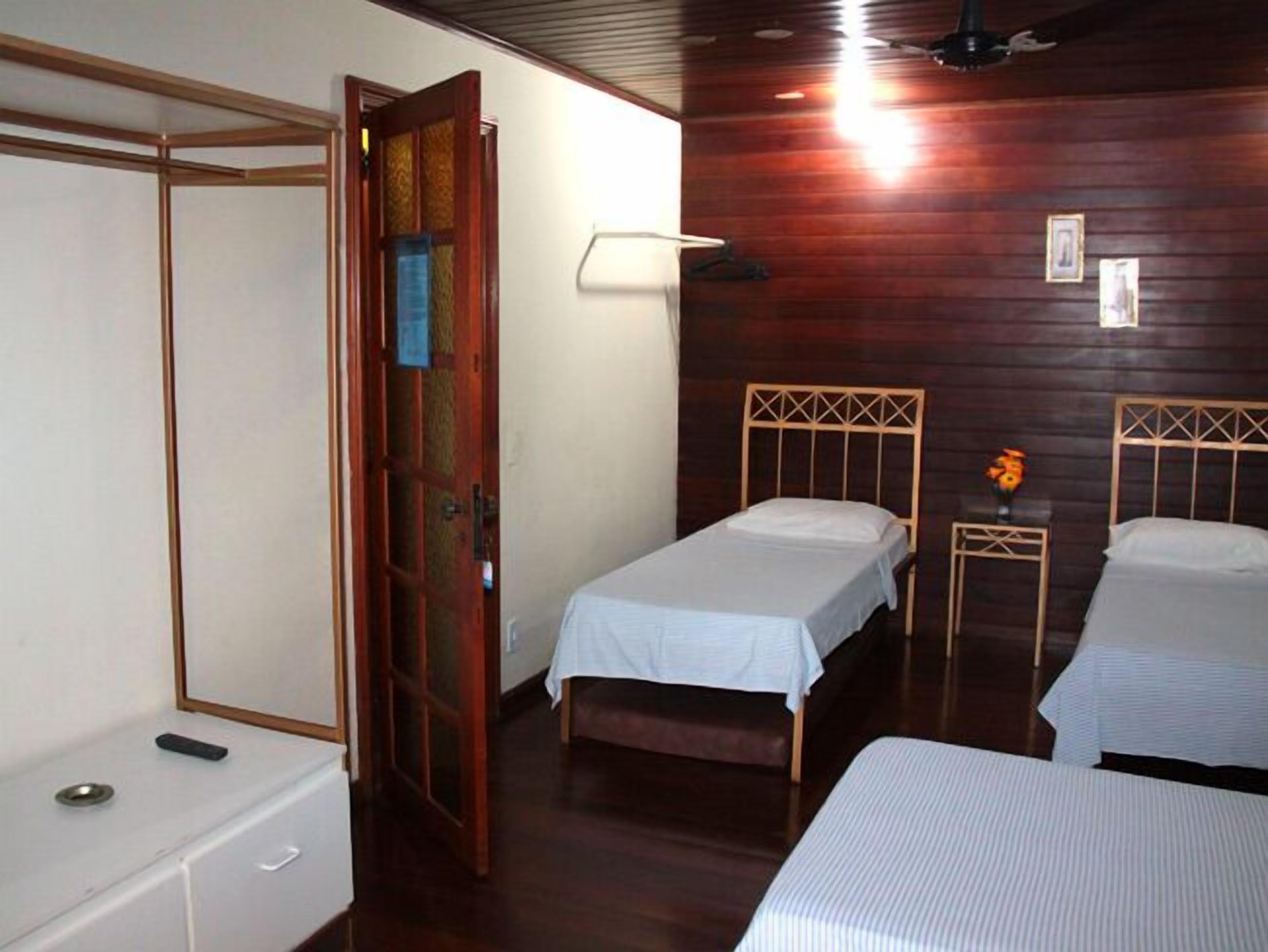 A room with two single beds, a wooden wardrobe, a small table with a lamp, and a door with a decorative panel.