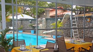 An outdoor dining area with tables and chairs, a pool, and a stone wall with a slide. - Pousada Praia da Costa (Vila Velha)