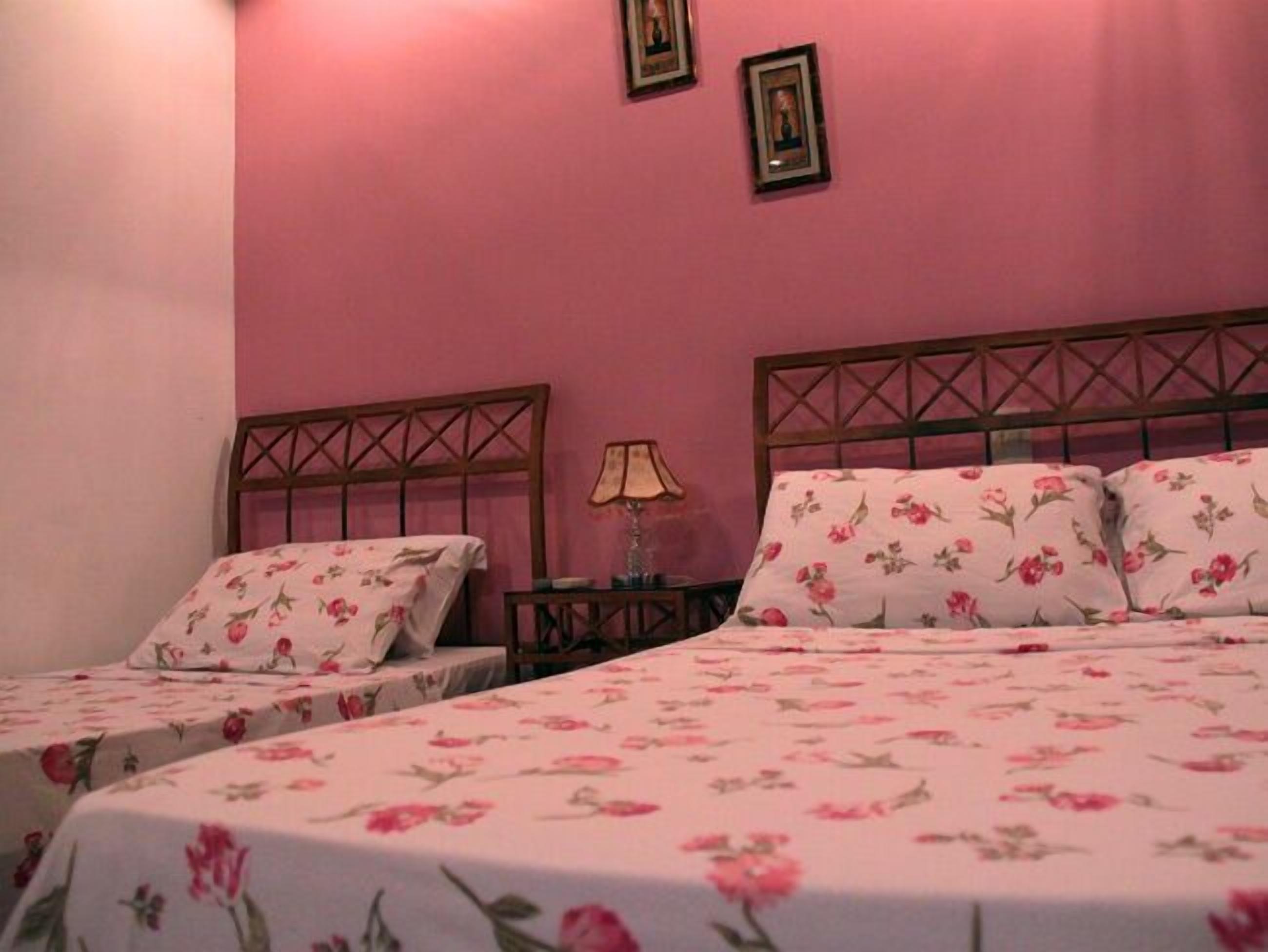 A room with two single beds, each with floral-patterned bedding, a wooden headboard, and a bedside table with a lamp.