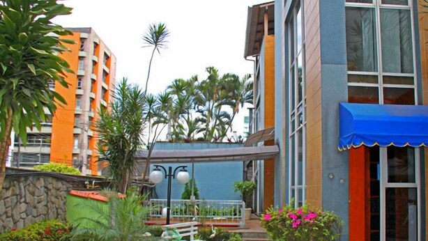 A hotel entrance with a stone pathway leading to a covered area, surrounded by lush greenery and palm trees. - Pousada Praia da Costa (Vila Velha)