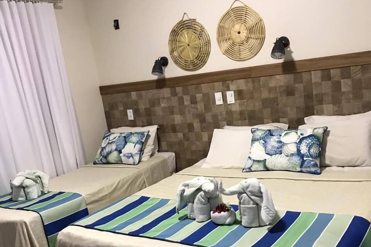 Habitación de hotel con dos camas, cada una con ropa de cama a rayas y almohadas decorativas. Se observan tapices en las paredes sobre las camas y una cortina a la izquierda.