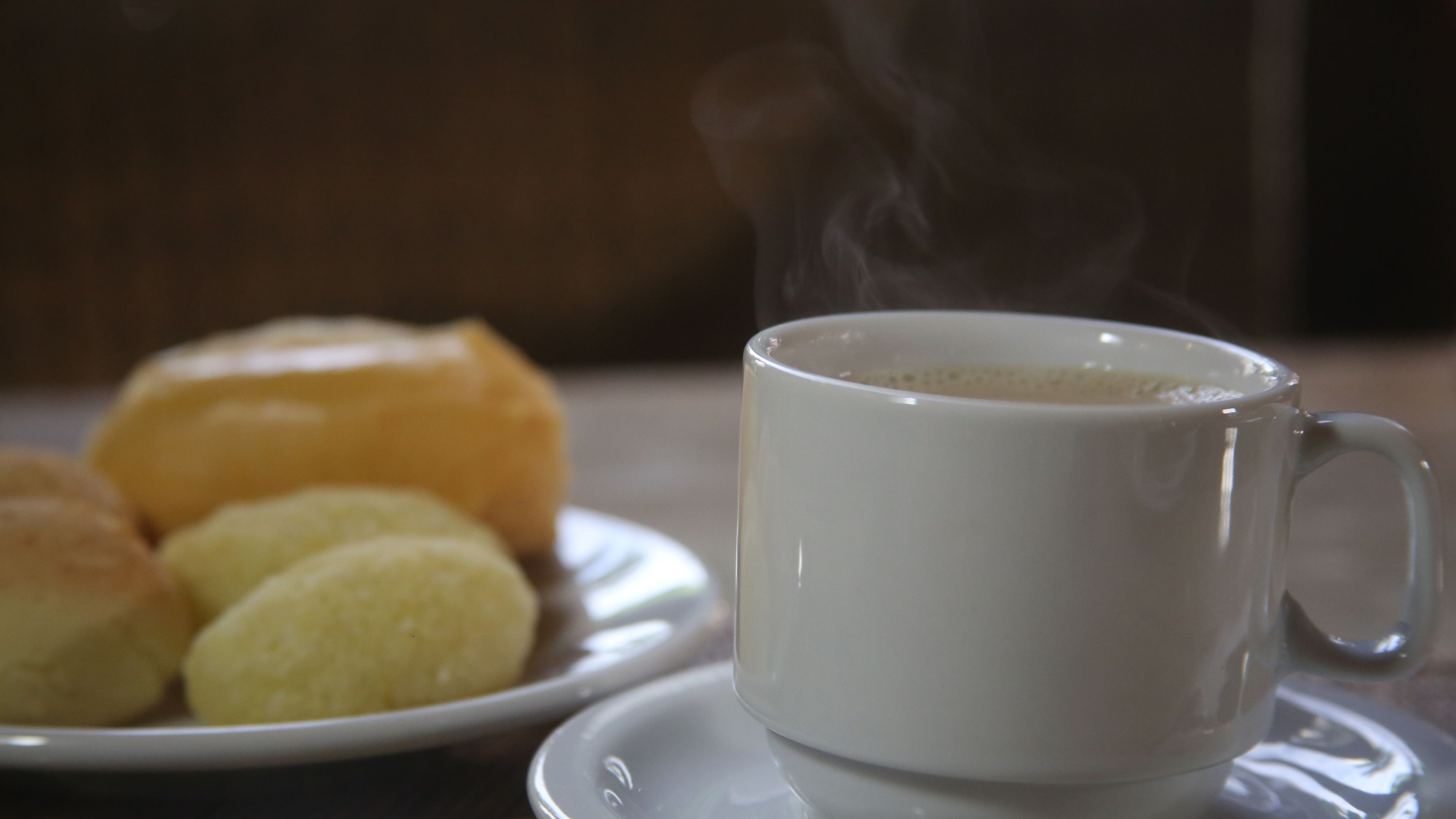 Höyryävä valkoinen kahvikuppi, lautanen, jossa on kaksi leivosta, ja muffinssi pöydällä.