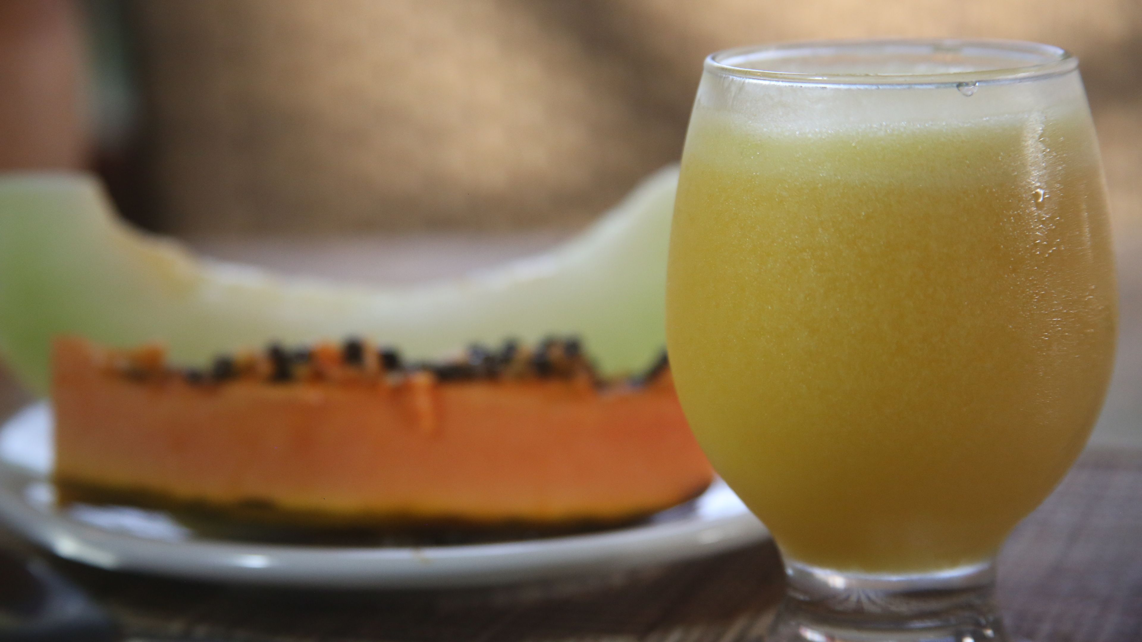 A glass of yellow beverage next to a sliced fruit on a plate.