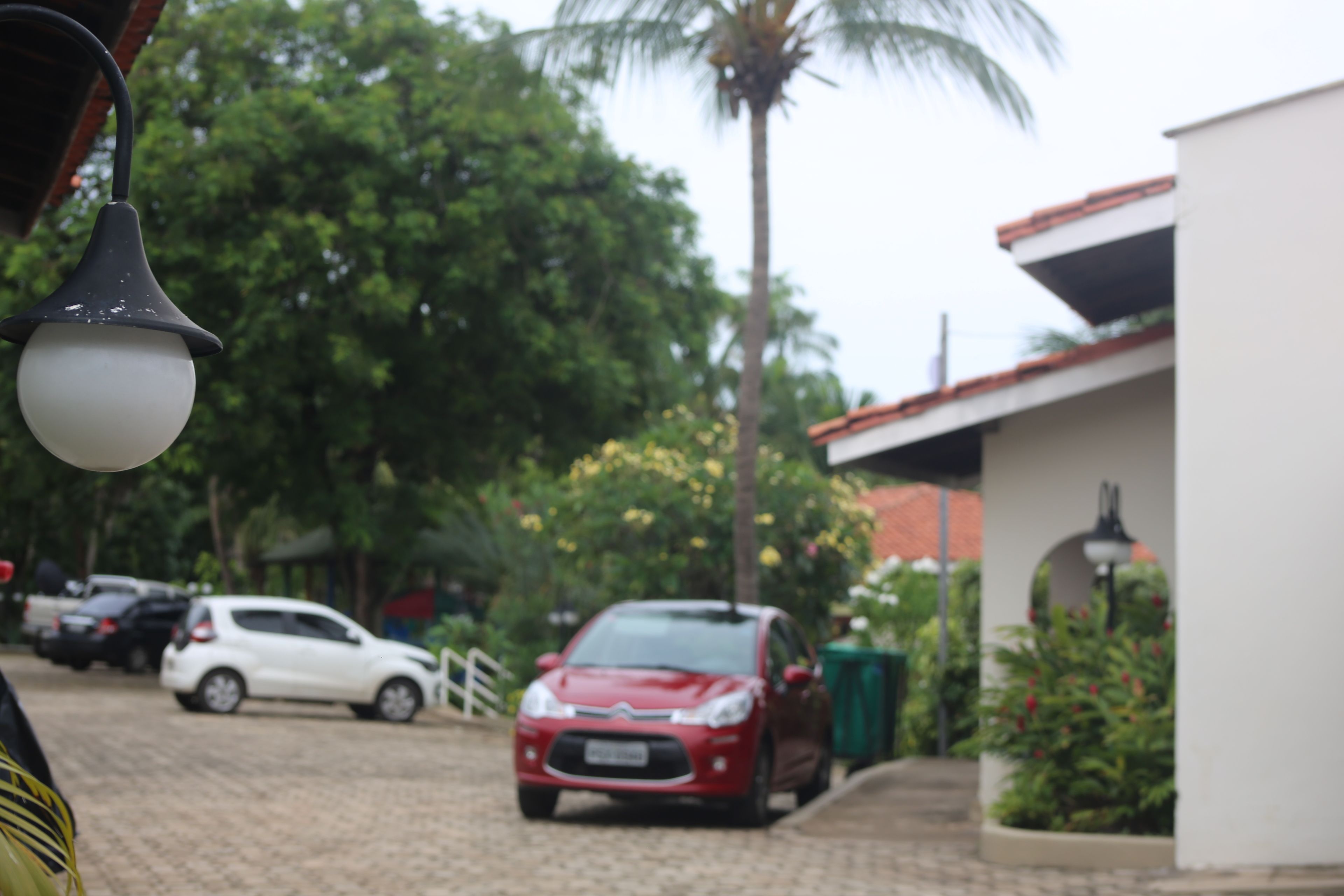 A red car parked in a driveway with a white building in the background.