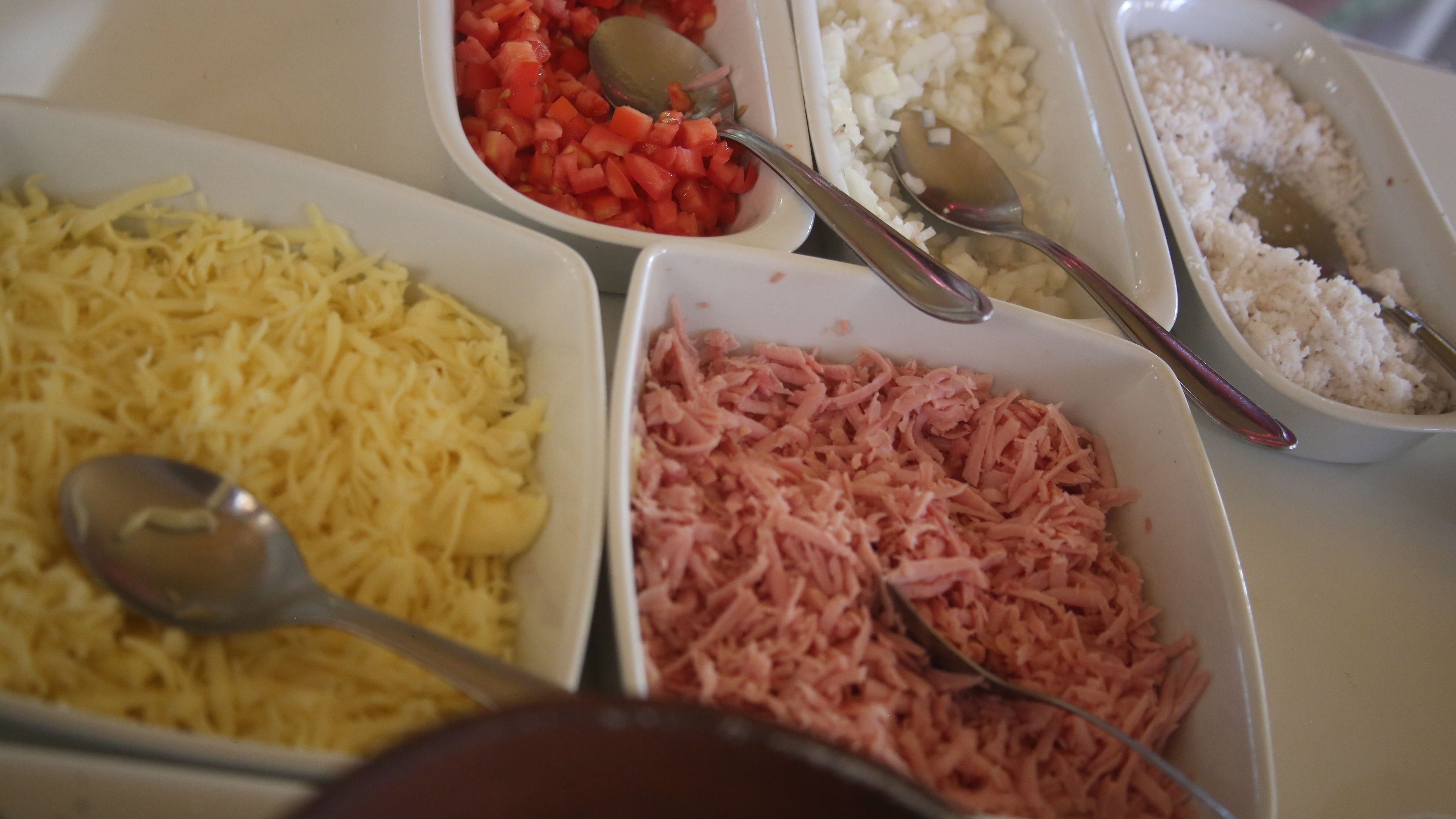 A table with four bowls containing shredded cheese, diced tomatoes, shredded ham, and cooked rice.