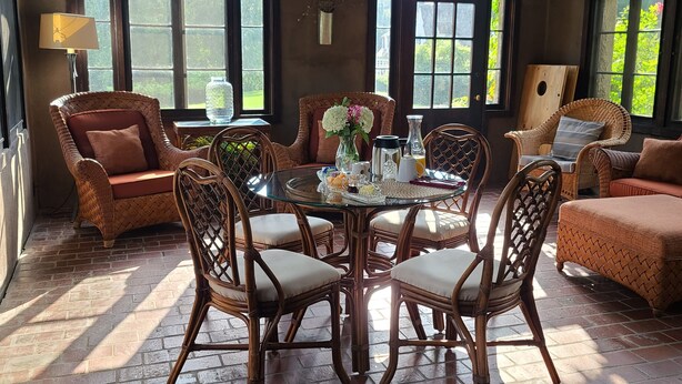 A room with a round table surrounded by wicker chairs, large arched windows, and a brick floor. - Four Mounds Inn (Dubuque)