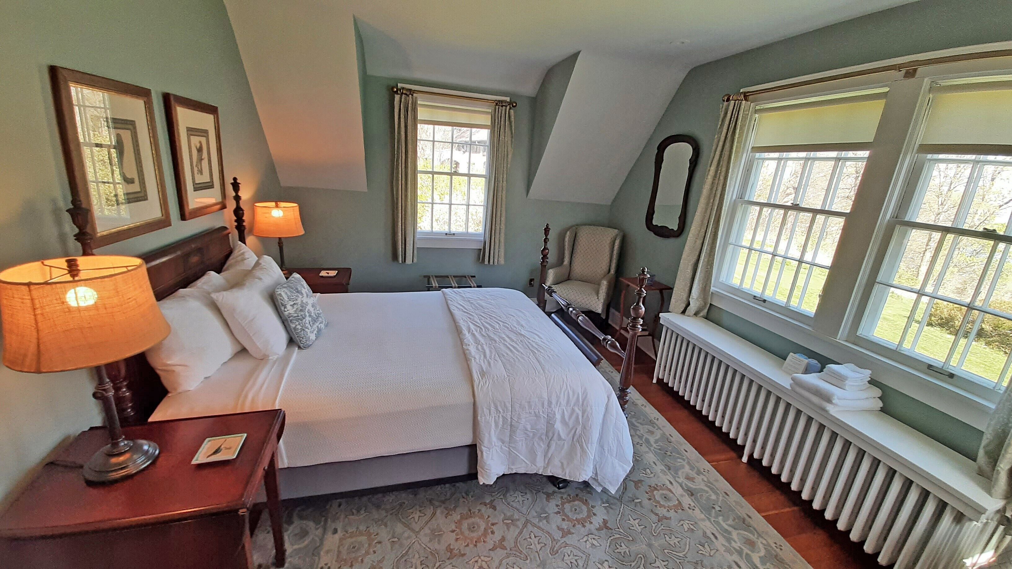A neatly arranged bedroom with a large bed, two bedside lamps, a chair, and a radiator.
