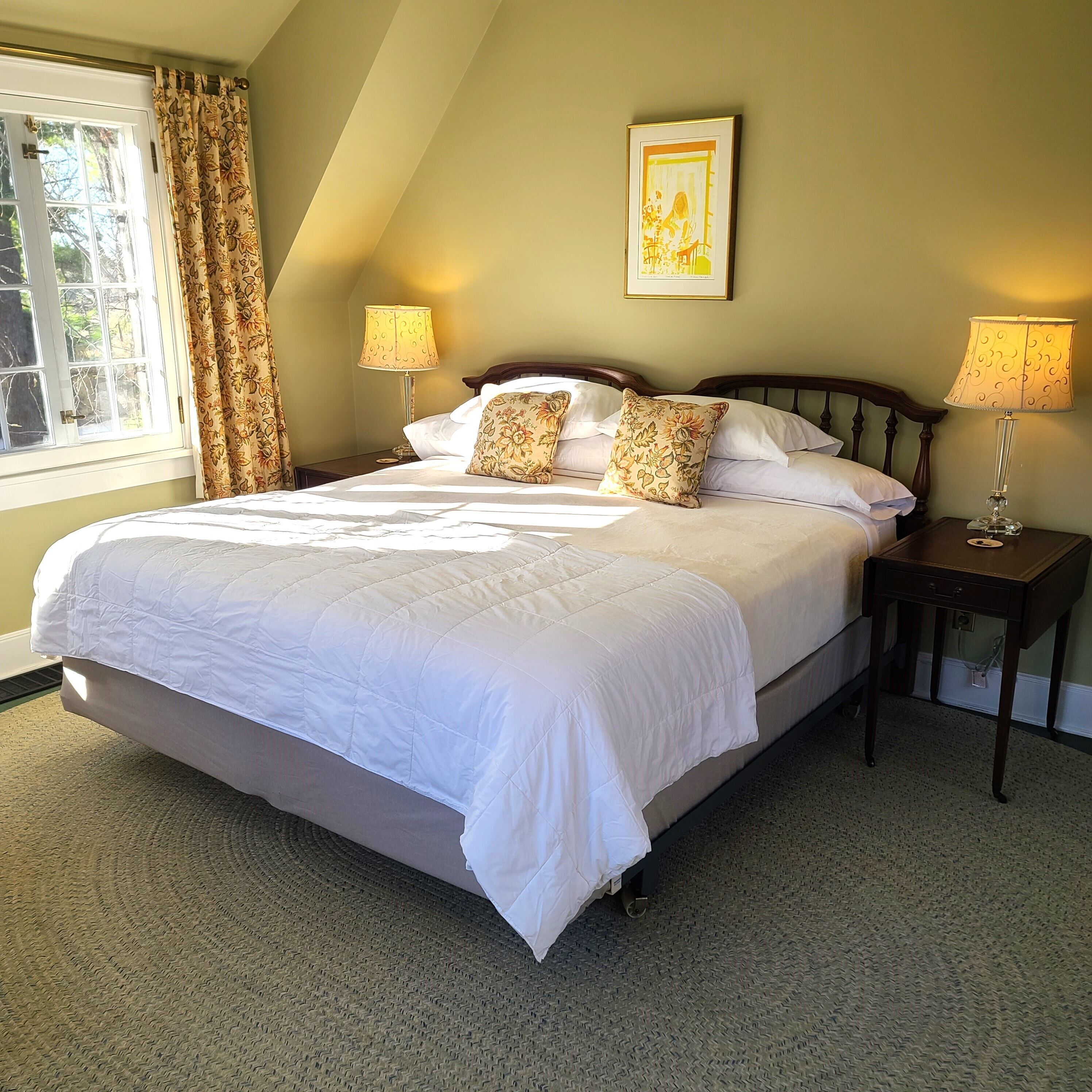A neatly made bed with white bedding, two bedside lamps, and a framed picture on the wall.